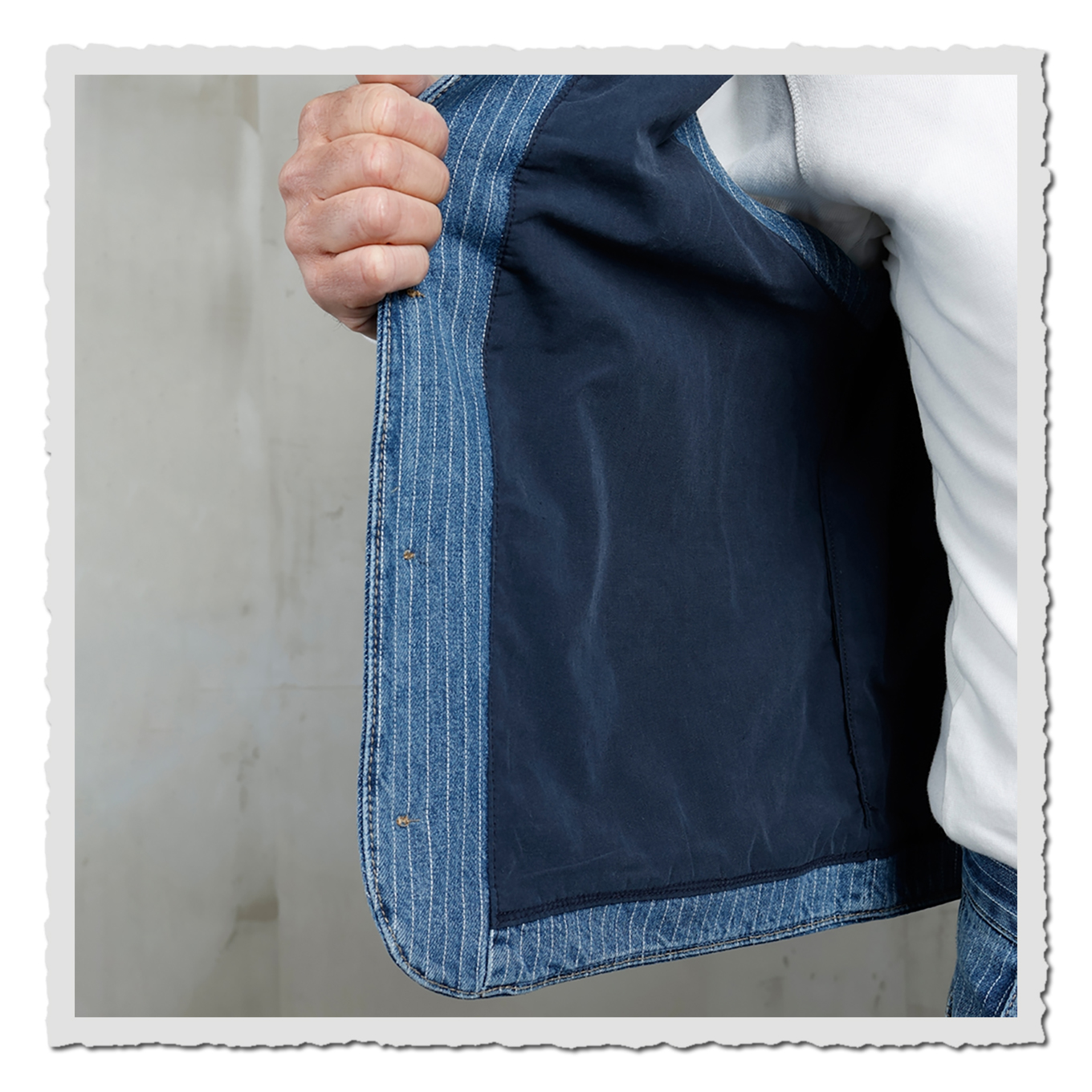 Detailfoto der geöffneten Weste: blau gestreifter Außenstoff und dunkles Innenfutter, Hand hält die Kante.